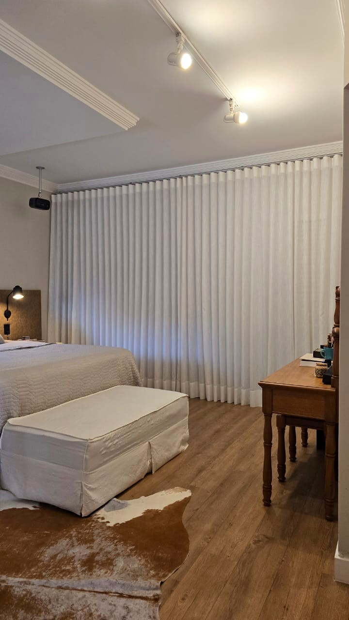 Quarto com cortina branca, cama e mobiliário em madeira